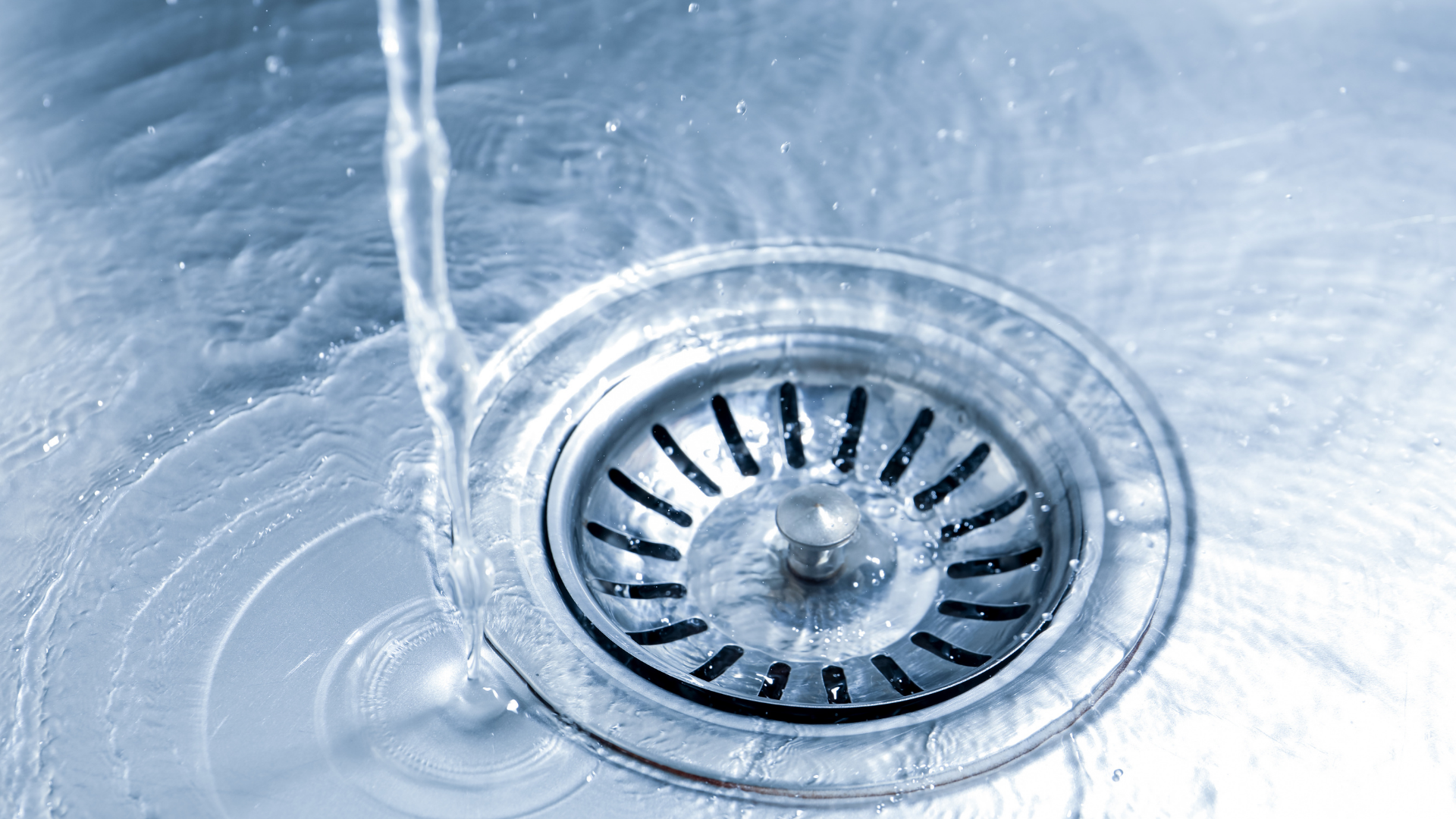 Water draining into a silver sink drain with rippling blue-tinted water