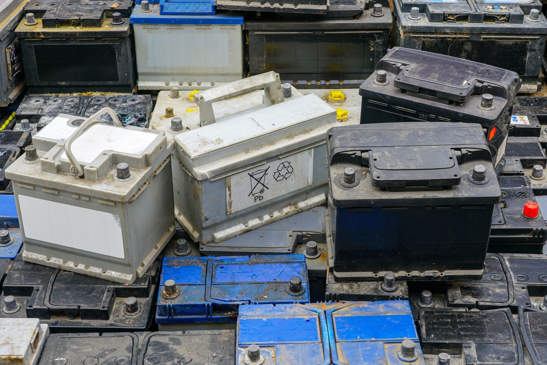 Stacked old car batteries in white, black, and blue on a cluttered surface.
