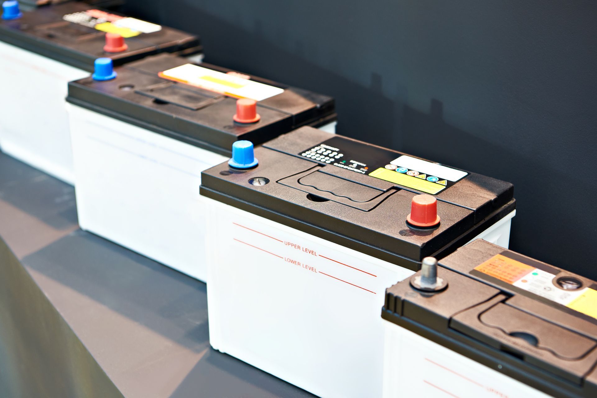 Row of automotive batteries with labeled tops displayed on a shelf.