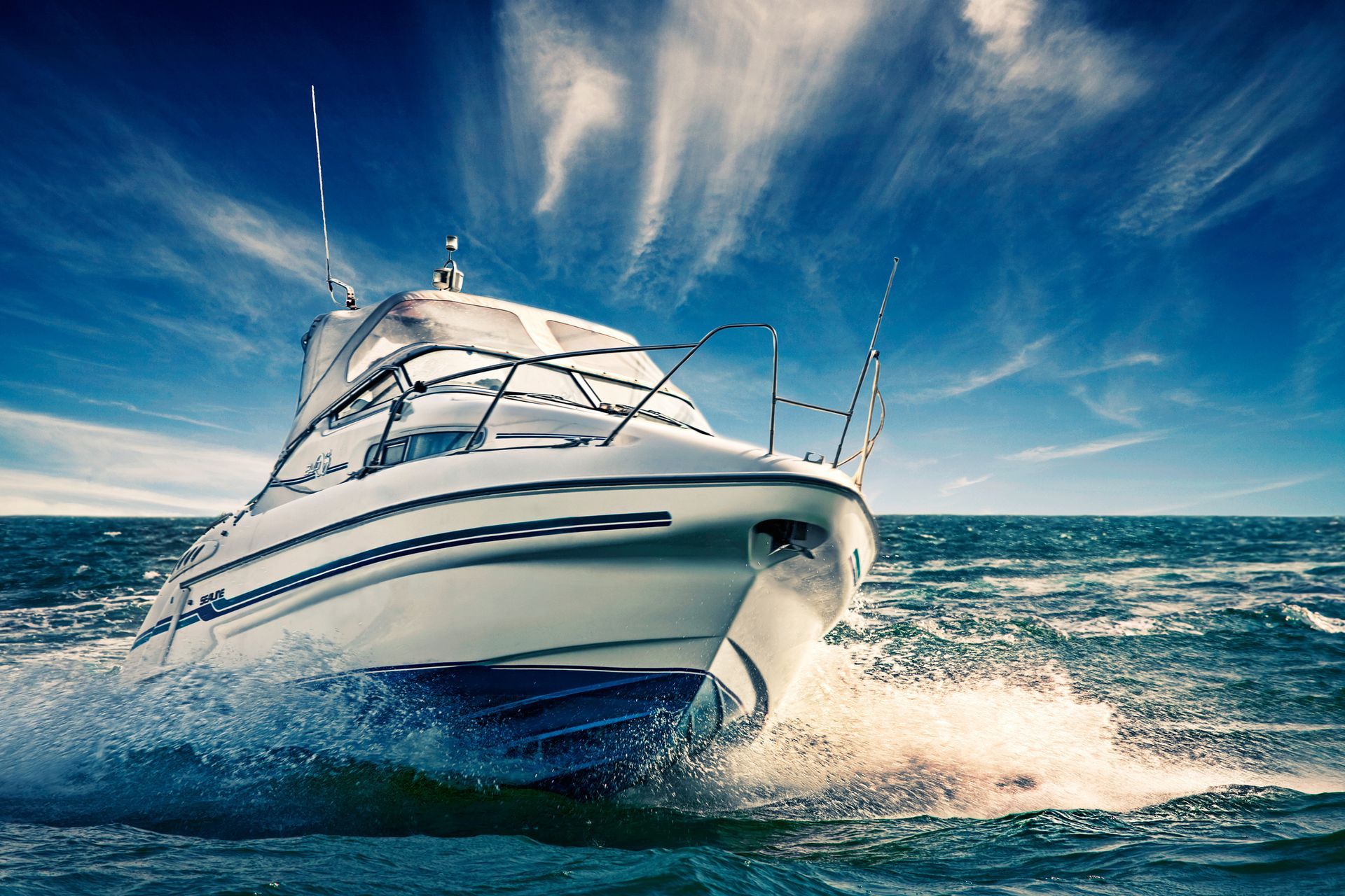 White motorboat speeding across blue water, creating white waves under a blue sky.