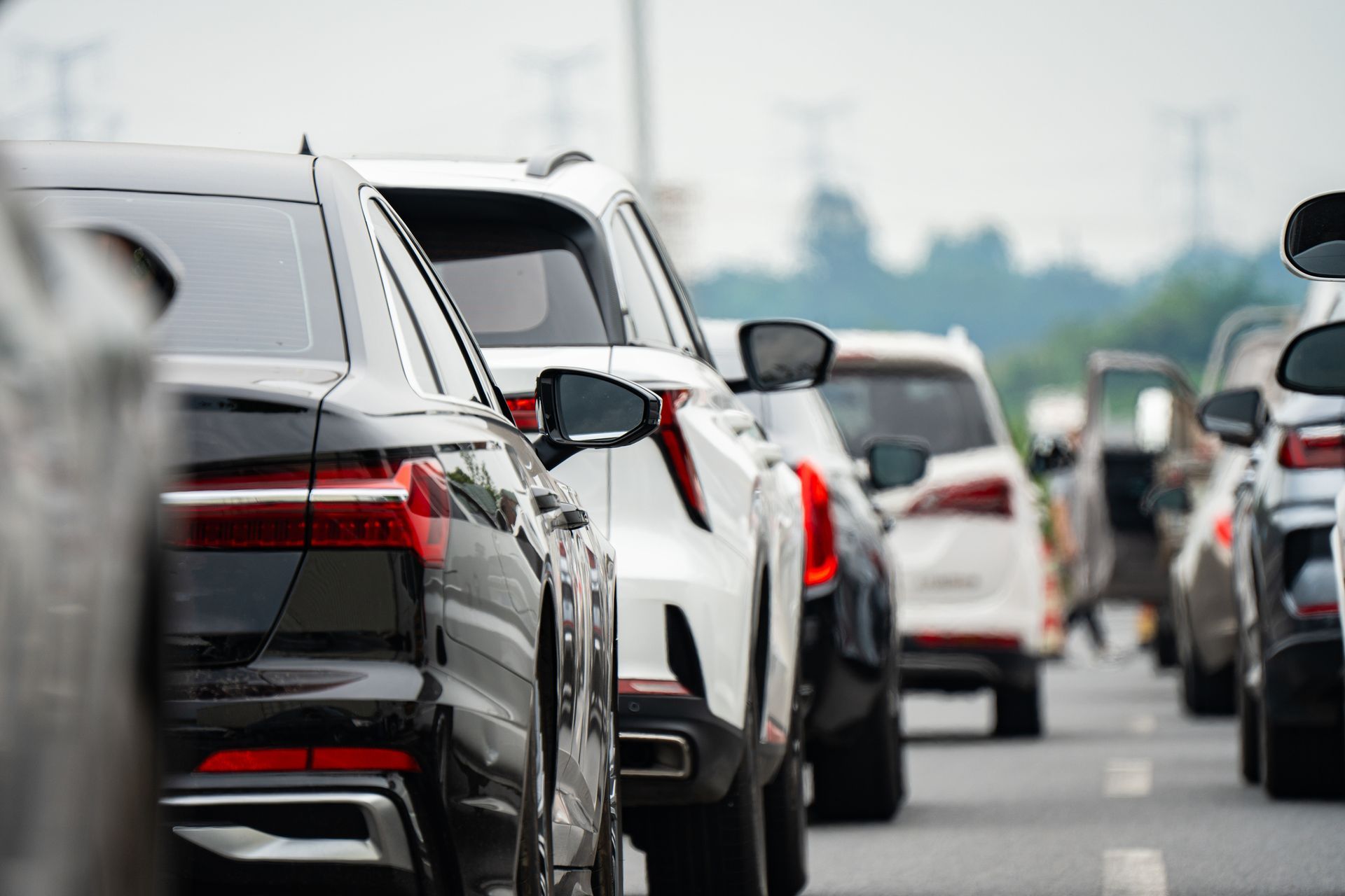 Cars in traffic on a multi-lane road, white and black vehicles, cloudy sky.