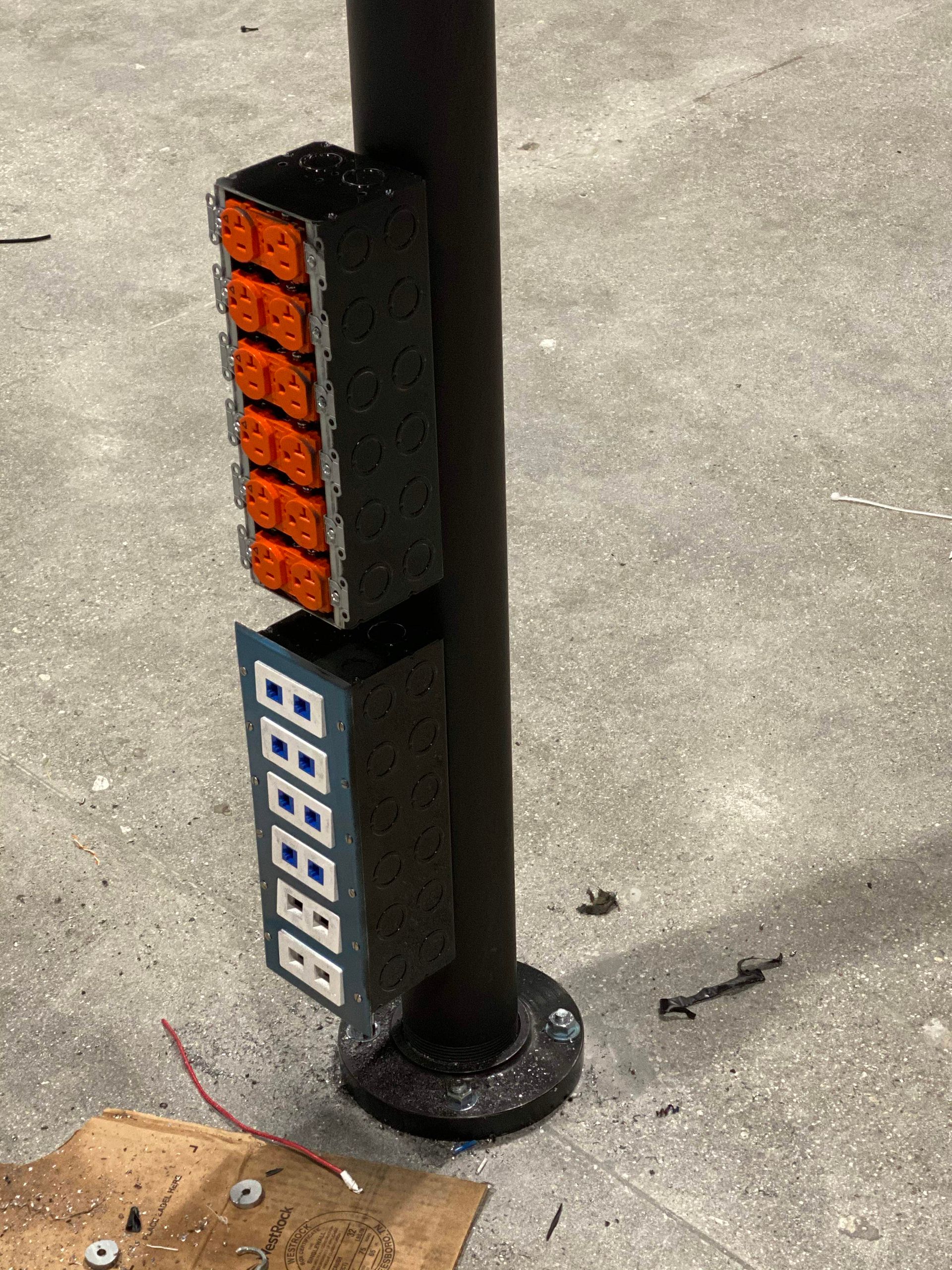 Black pole with stacked orange and blue marker blocks beside a concrete path