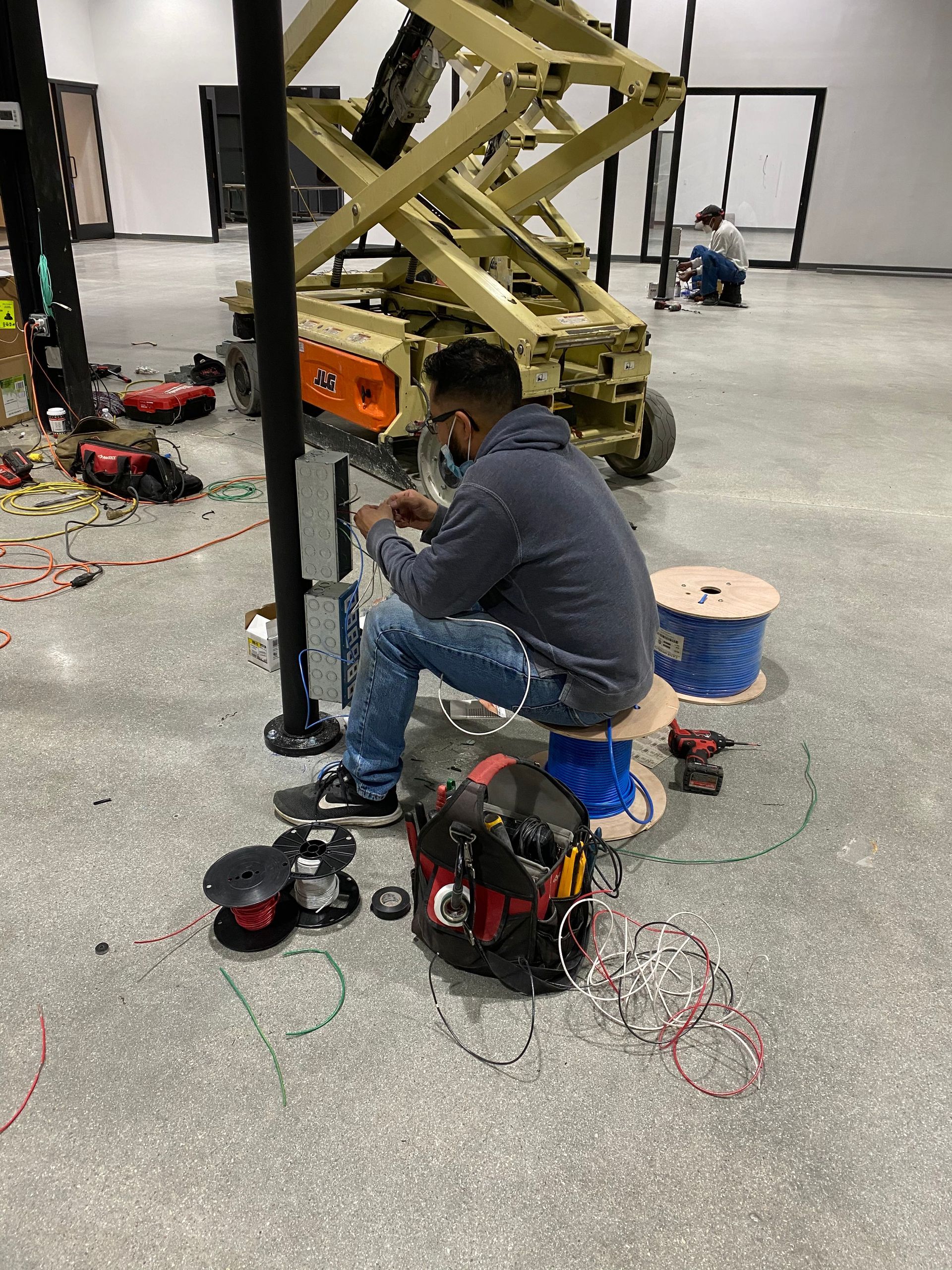Technician working on equipment in a workshop, surrounded by tools and cables on the floor