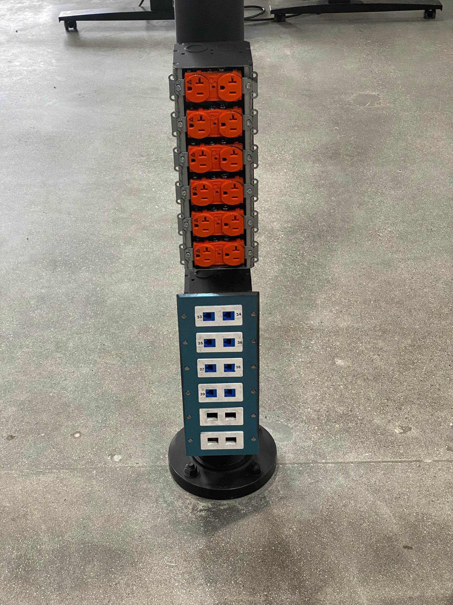 Close-up of a black pole with orange and blue button panels on a concrete floor