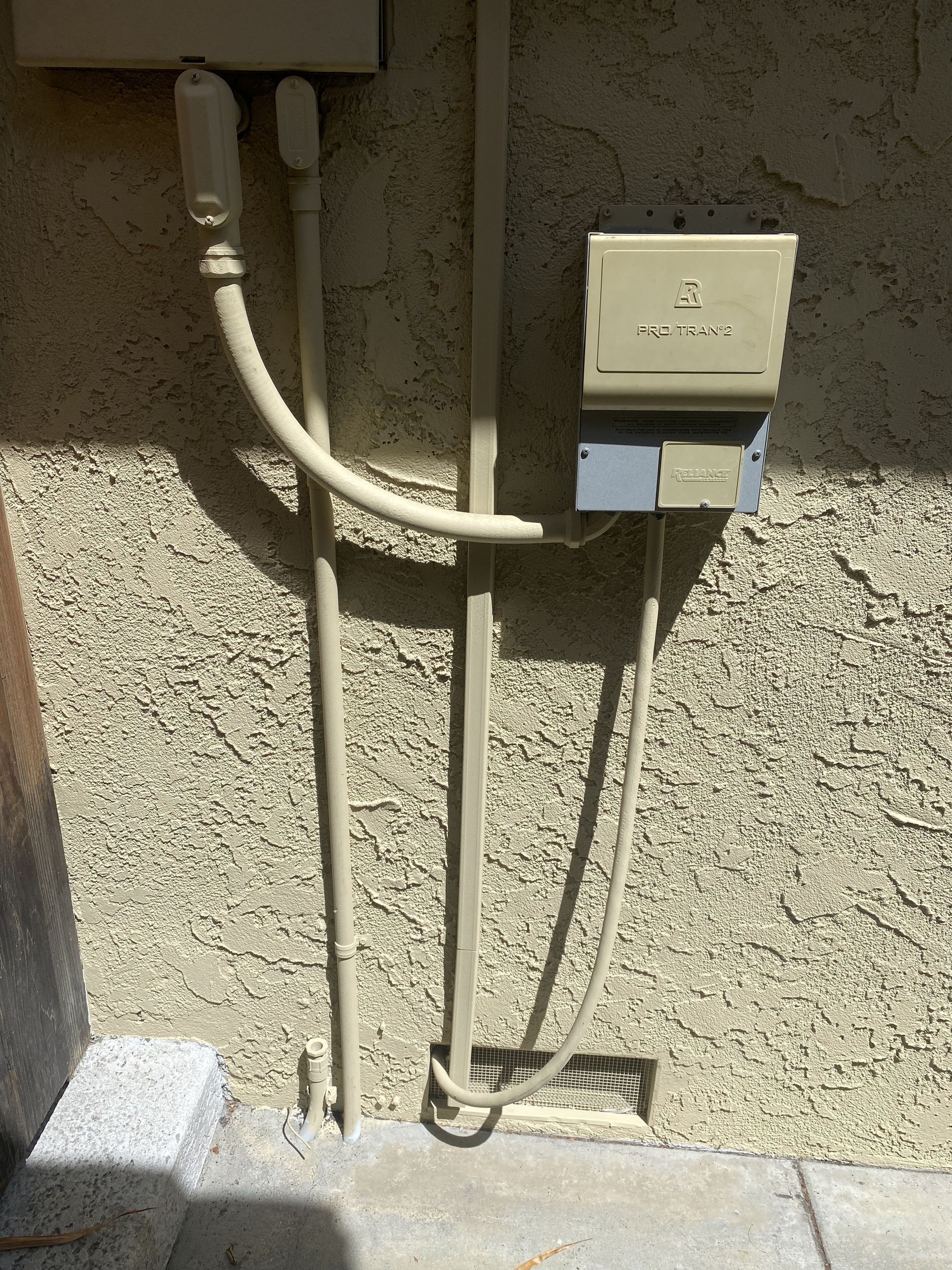 Outdoor stucco wall with electrical box and exposed conduit pipes in sunlight