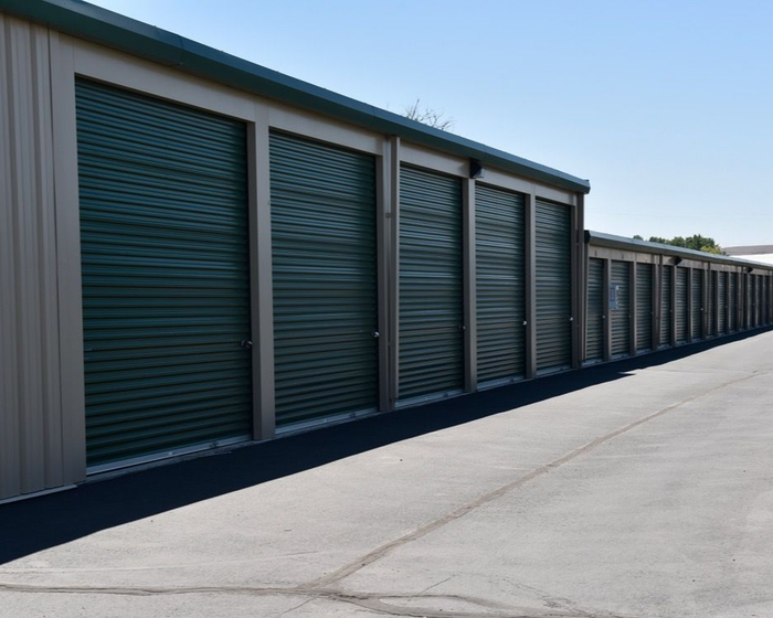 Row of green storage unit doors along a long concrete driveway under a clear sky