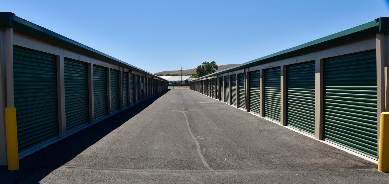 A row of green storage units are lined up on the side of a road.
