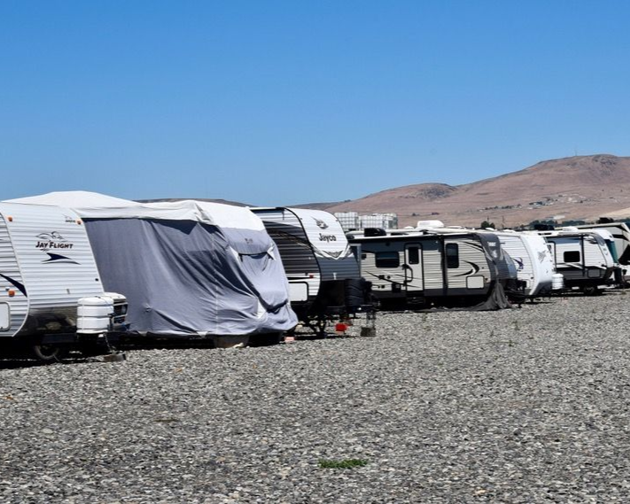 Row of parked RVs and campers on a gravel lot with desert hills in the background