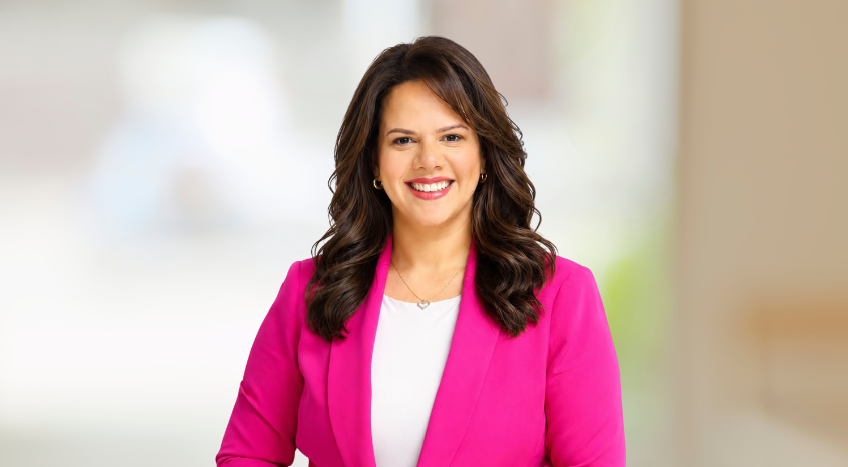 Smiling woman in a bright pink blazer against a softly blurred background