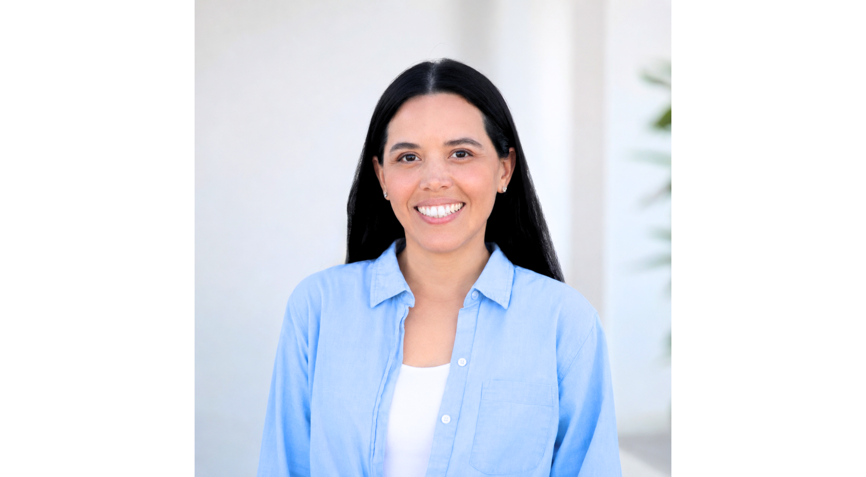 Smiling person in a light blue shirt standing against a bright white background