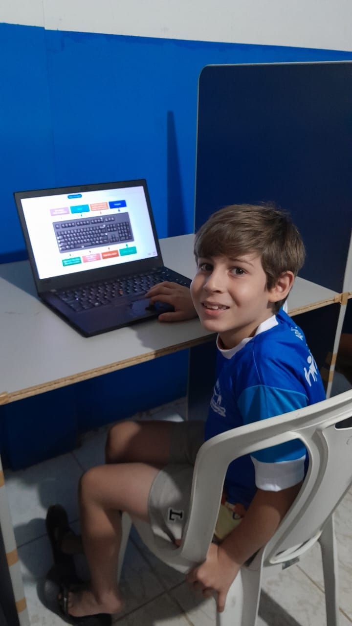 Uma pessoa vestindo uma camisa azul está sentada em uma mesa usando um laptop com um teclado na tela.