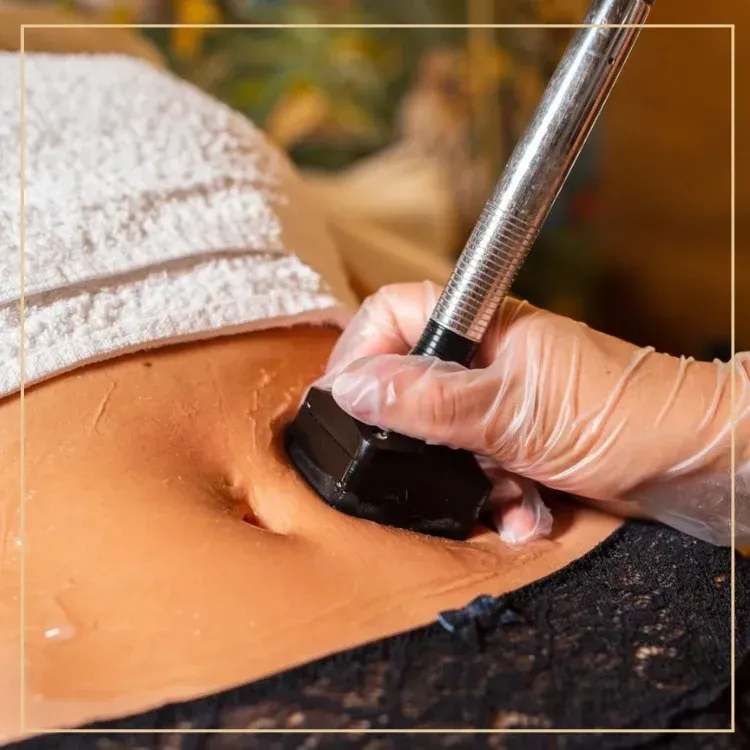 A gloved hand uses a handheld aesthetic ultrasound wand to perform a cosmetic treatment on a person's abdomen.
