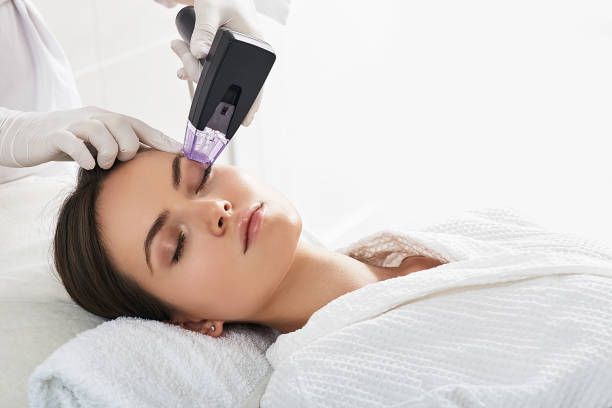 A professional performing a cosmetic skin treatment on a patient's forehead using a handheld device in a clinical setting.