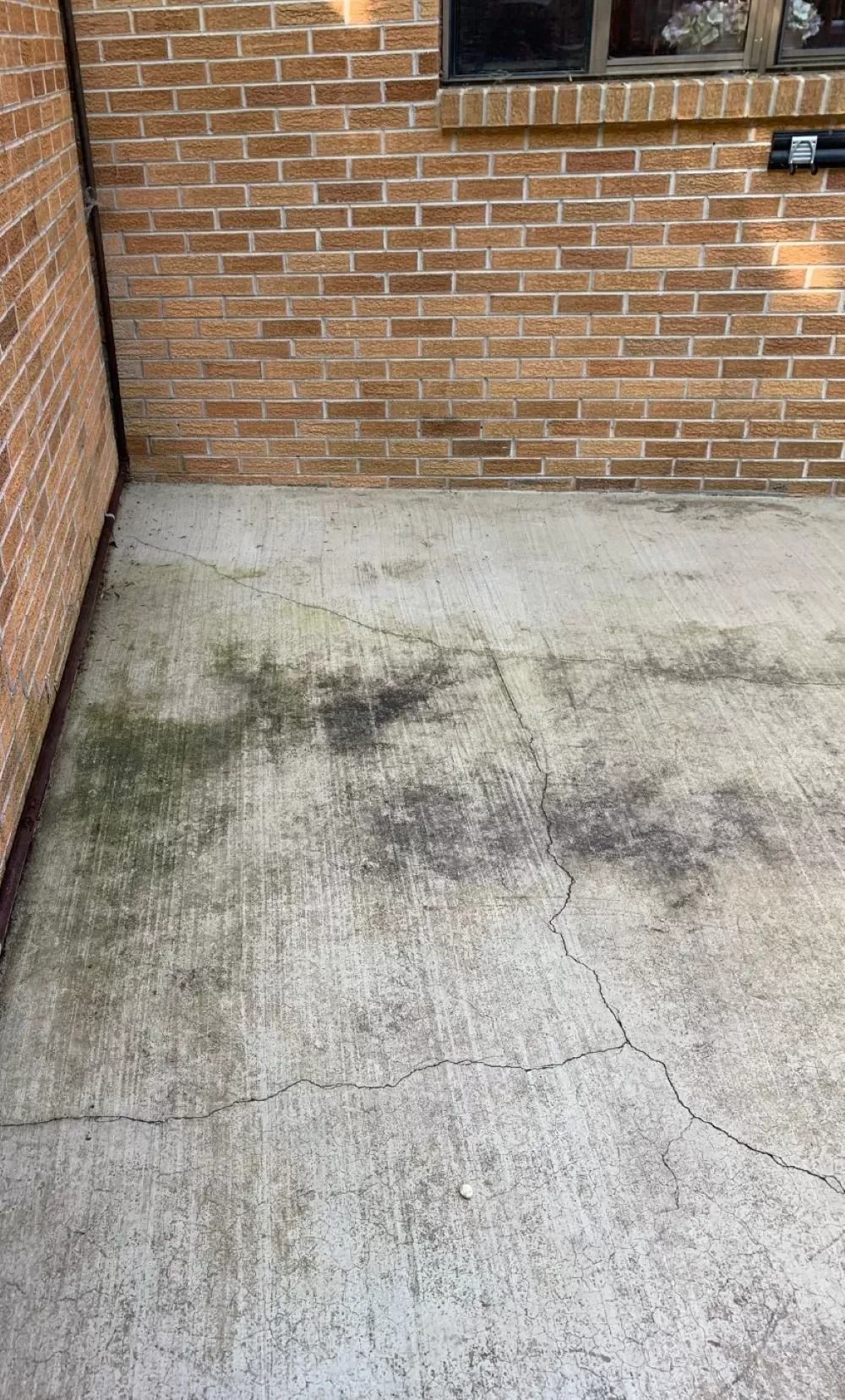 Brick wall and concrete patio with dark stains and cracks.