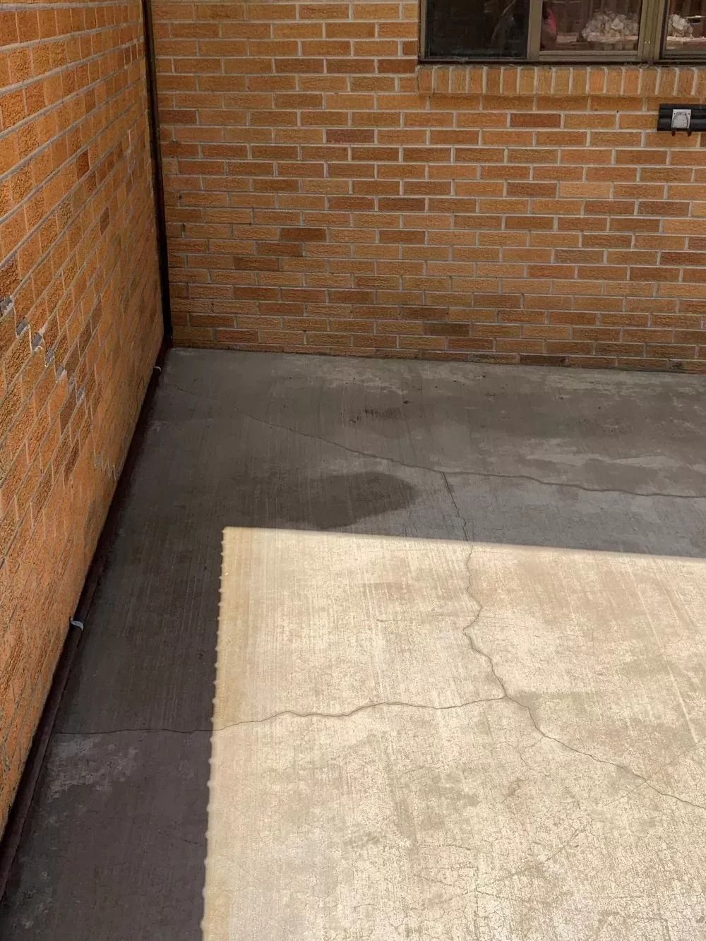 Brick-walled outdoor corner with concrete floor and a beige mat in sunlight