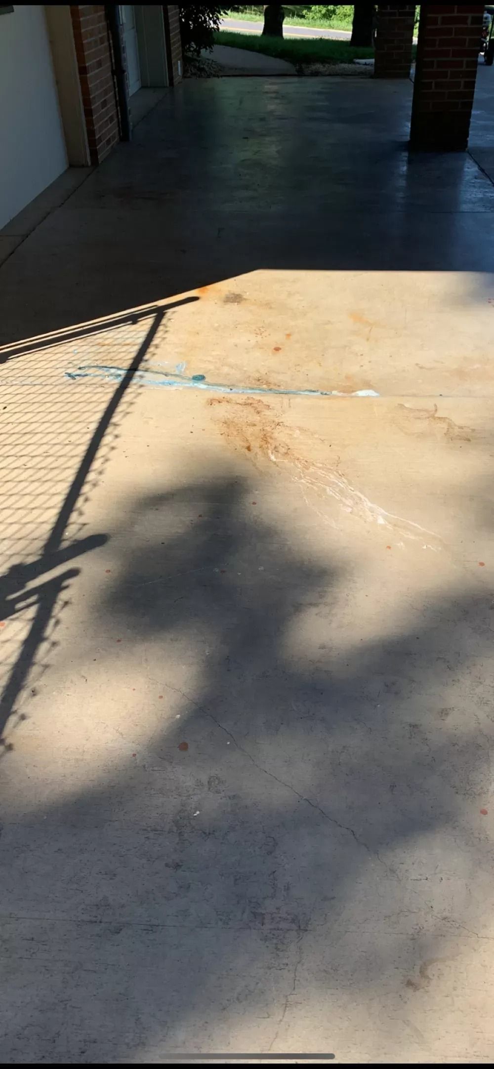 Concrete driveway in bright sunlight leading into a shaded garage or carport, with tree shadows across it