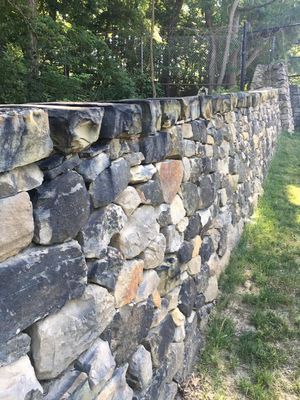 A large stone wall is surrounded by grass and trees.