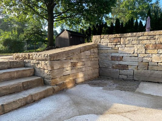 A stone wall with stairs leading up to it and a shed in the background.