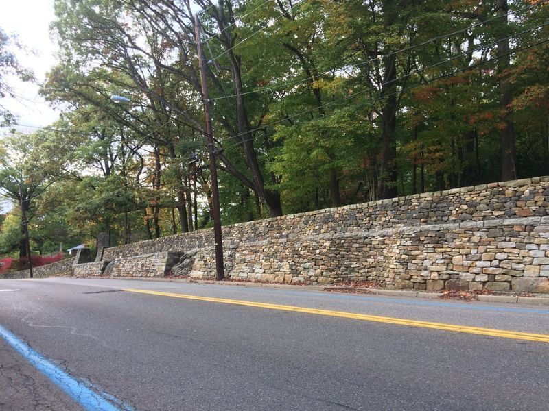 A stone wall along the side of a road surrounded by trees