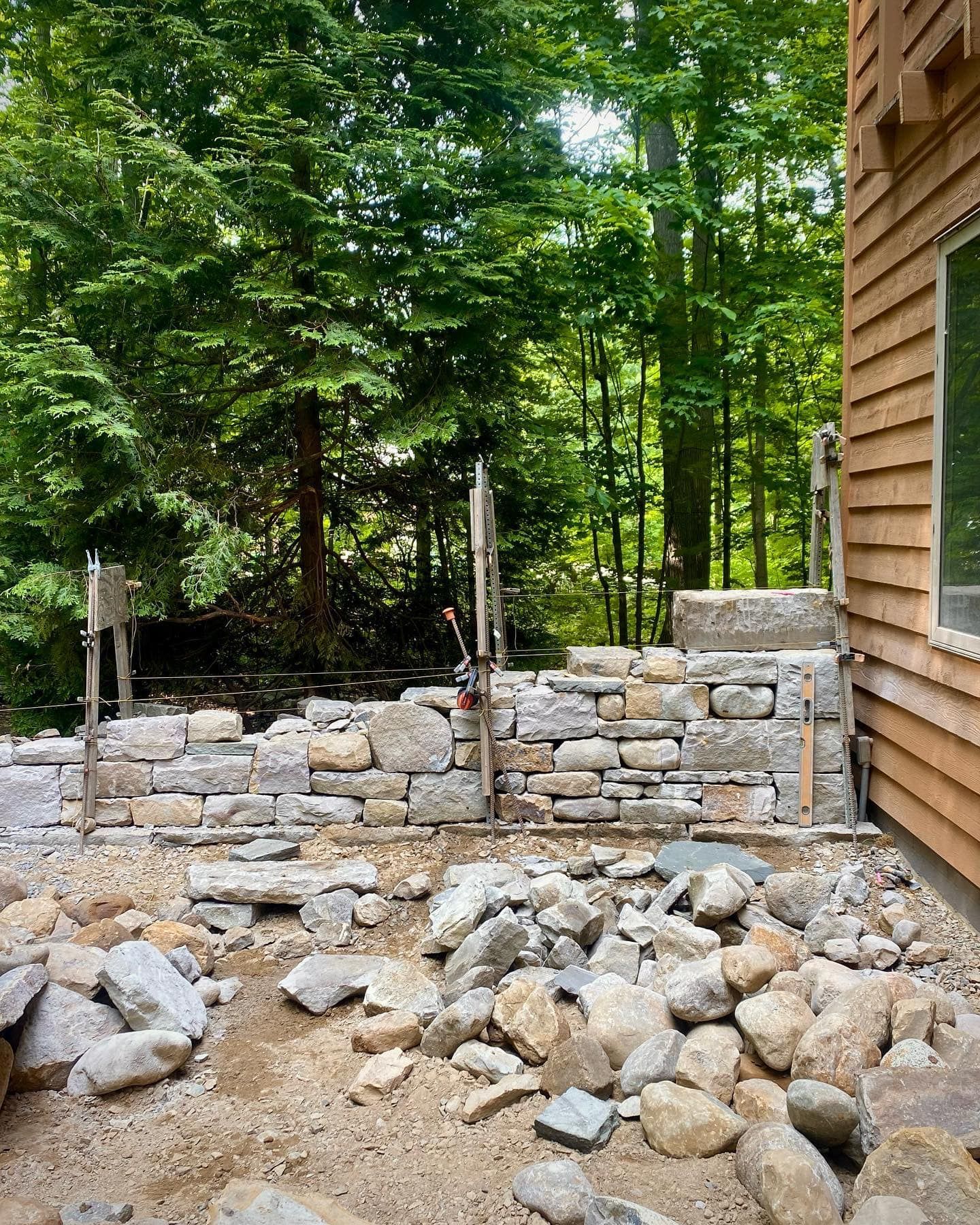 A stone wall is being built in front of a house in the woods.