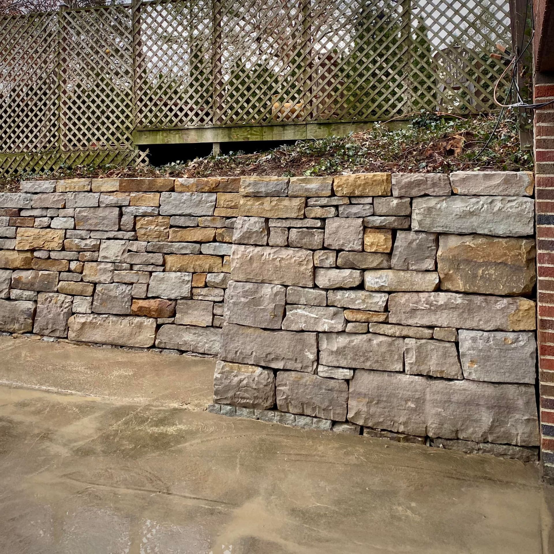 A stone wall with a lattice fence in the background