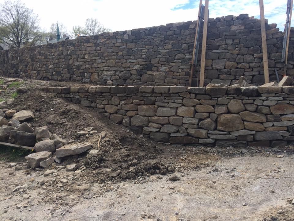 A large stone wall is being built in a dirt field.
