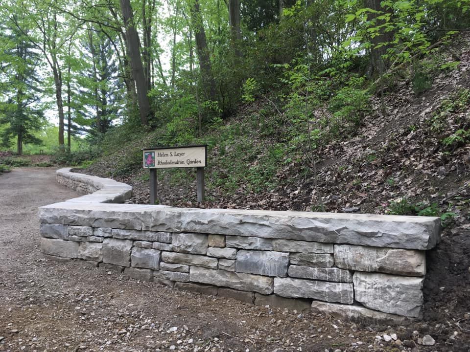 A stone wall with a sign on it in the woods.