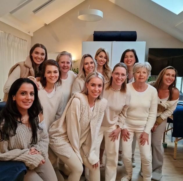 Een groep vrouwen in een lichtgekleurde kamer; lachend, in witte kleding, poserend voor een foto.