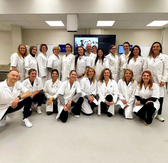 Een groep mensen in laboratoriumjassen poseert lachend in een laboratoriumomgeving.