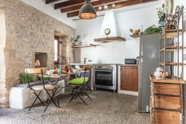 Bucătăria modernă a vilei din Mallorca, cu perete interior din piatră și mobilă vintage recondiționată. Ideală pentru un grup de 4-6 persoane care își doresc să gătească în timpul vacanței. 