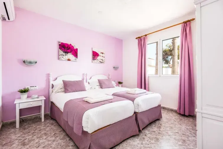 Un alt dormitor al vilei Ingrid din Menorca, cu pereți, draperii și așternuturi roz. Are două paturi de o persoană care pot fi despărțite sau alăturate.