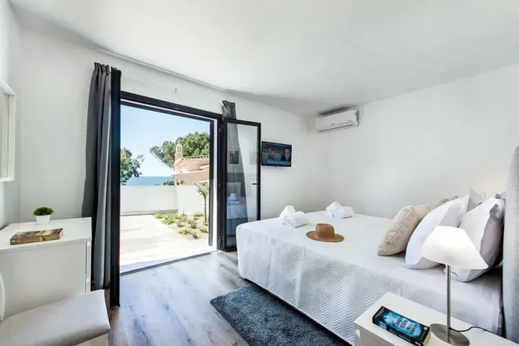 Vedere interioară a unei dintre camerele Vilei Maria Luisa din Algarve, cu televizor, aer condiționat, și balcon deschis cu vedere panoramică spre mare.