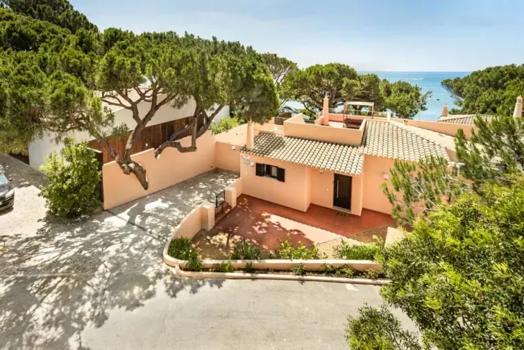 Vedere stradală cu vila Maria Luisa din Algarve, cu o construcție joasă și  gard colorat. Vila e înconjurată de vegetație mediteraneană și oferă priveliște directă spre mare. 