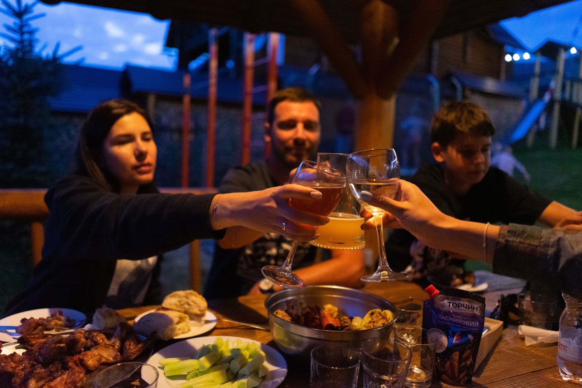 Un grup de prieteni pe terasa vilei lor de vacanță, luând cina și ciocnind un pahar de vin la apus.