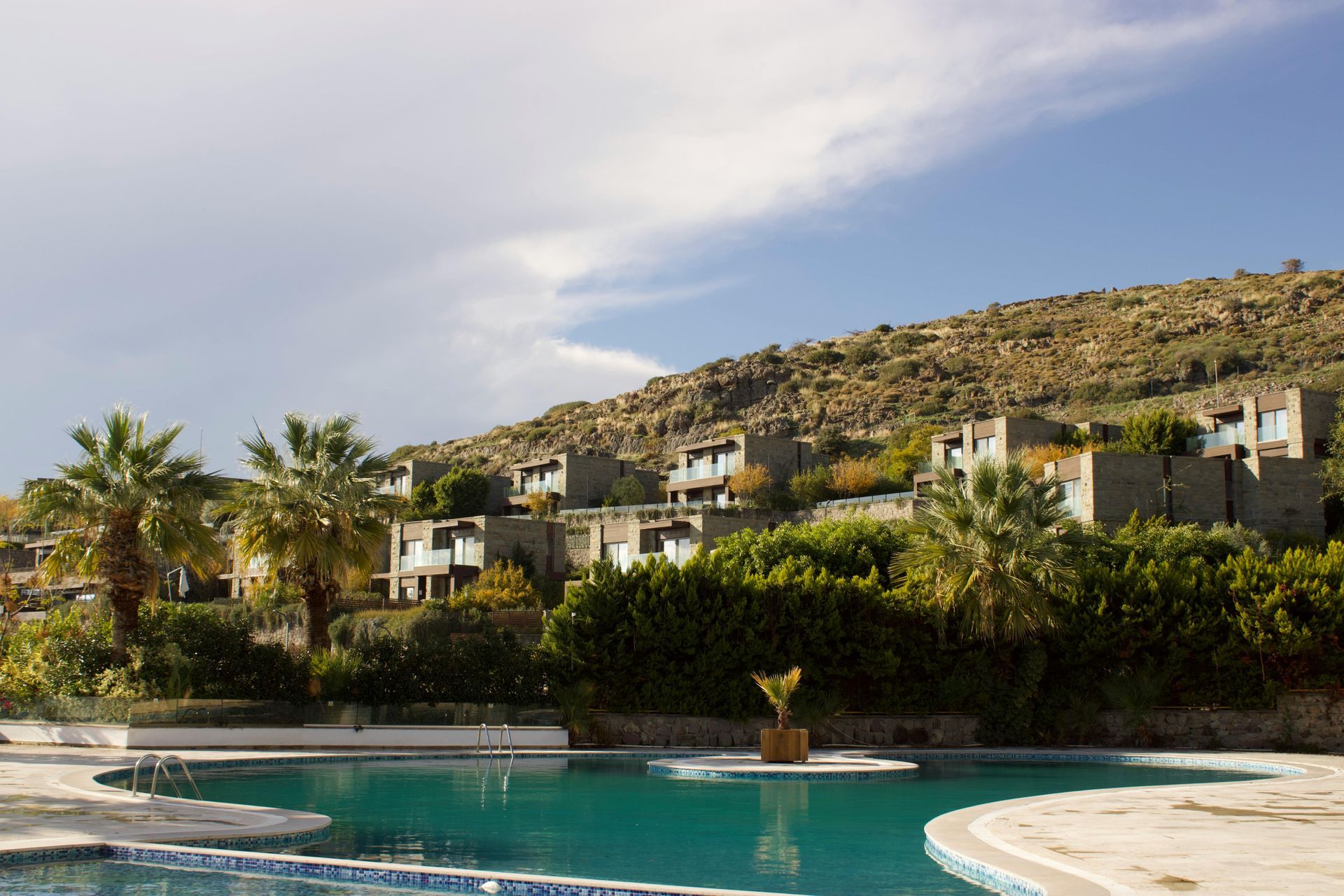Vila de vacanță cu piscină construită pe relieful deluros din Rhodos, Grecia. Piscina privată este în prim plan, iar vila cu palmieri în fundal.