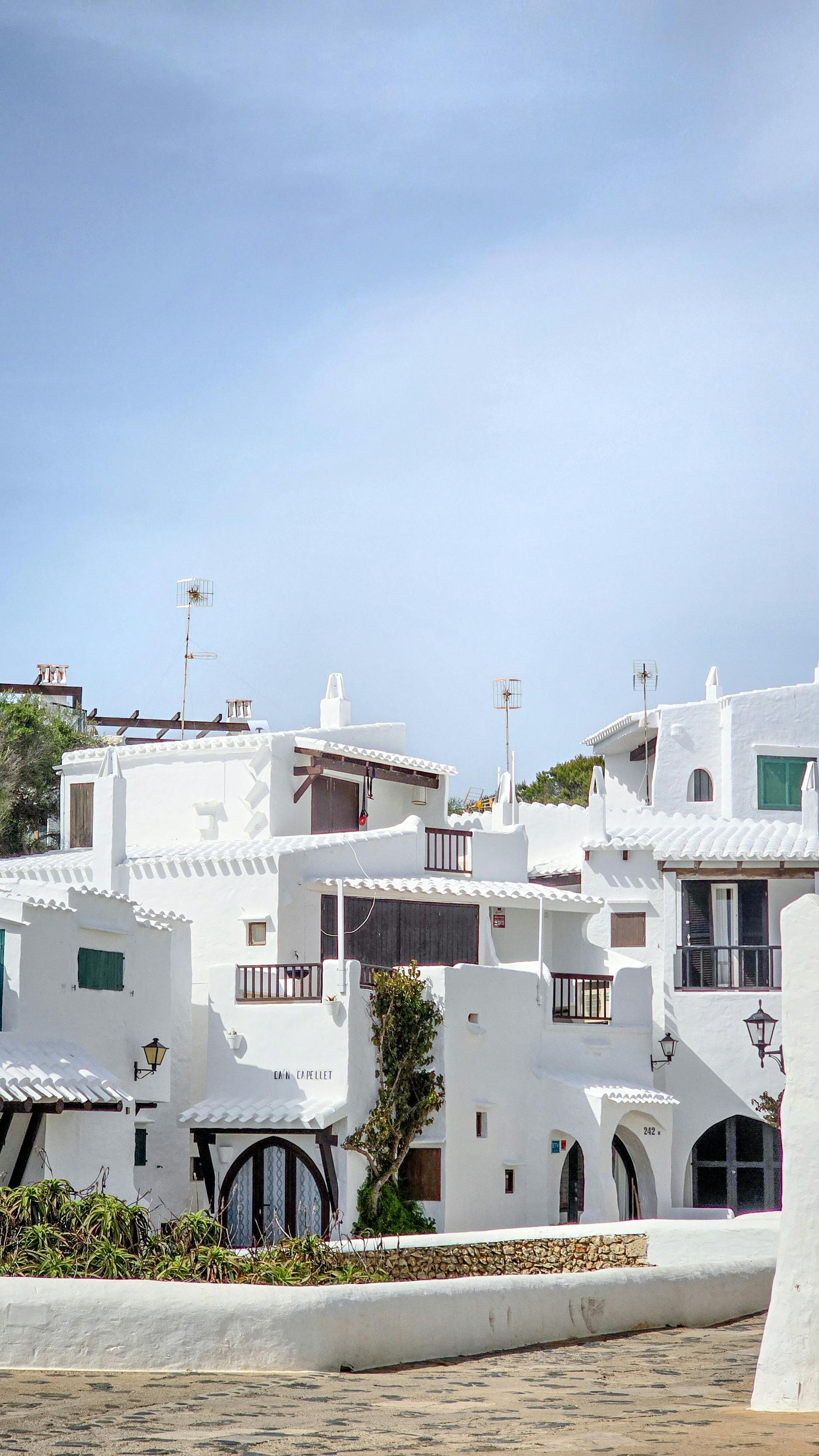 Vila de vacanță din Menorca, Spania. În prim plan este vila cu un design pitoresc, pereți văruiți în alb și geamuri colorate și înguste. 