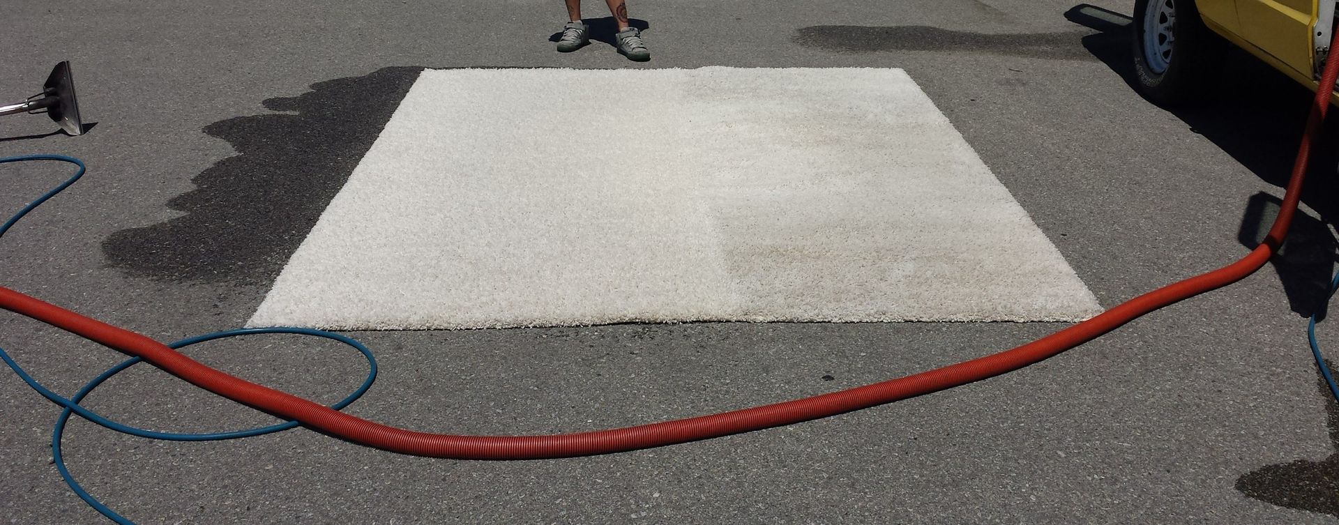 Workers painting a white rectangular road marking on asphalt with a red hose across the foreground