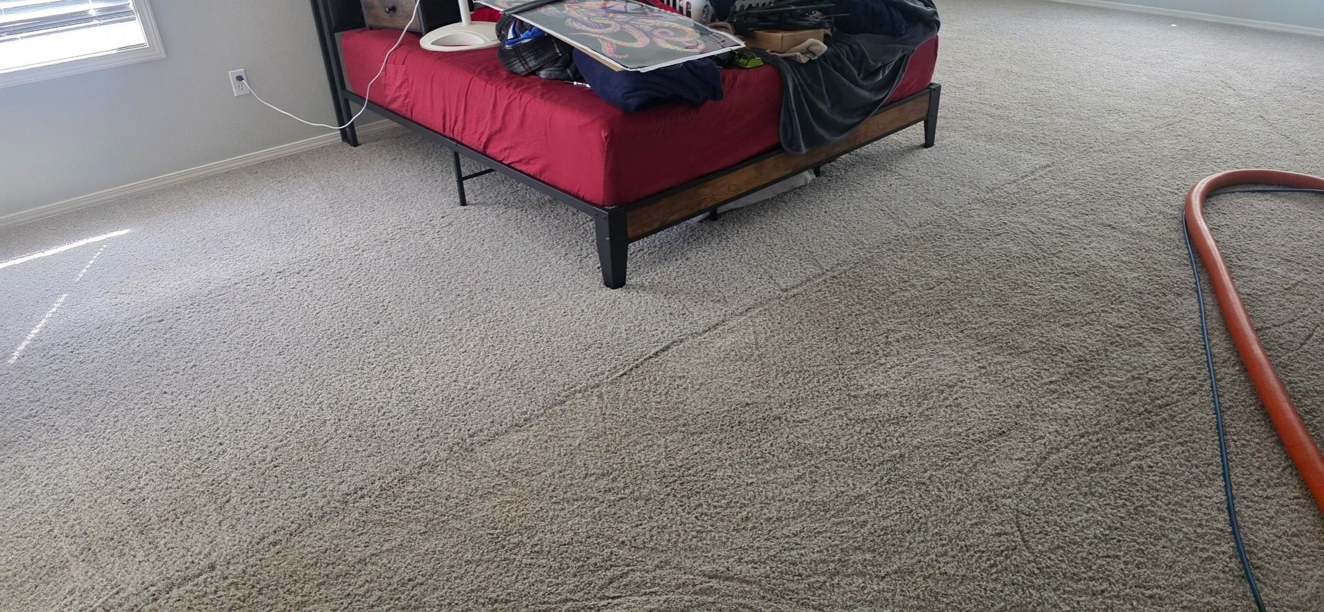 Living room carpet with a red daybed, patterned blanket, and an orange cord on the floor
