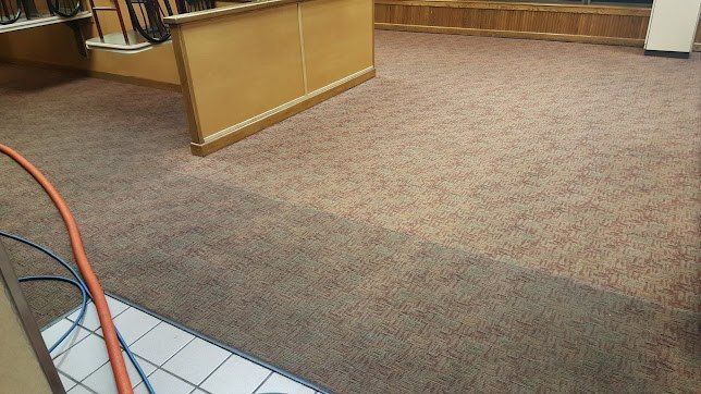 Carpeted office lobby with a wooden reception desk and tile floor corner, with cables visible in the foreground