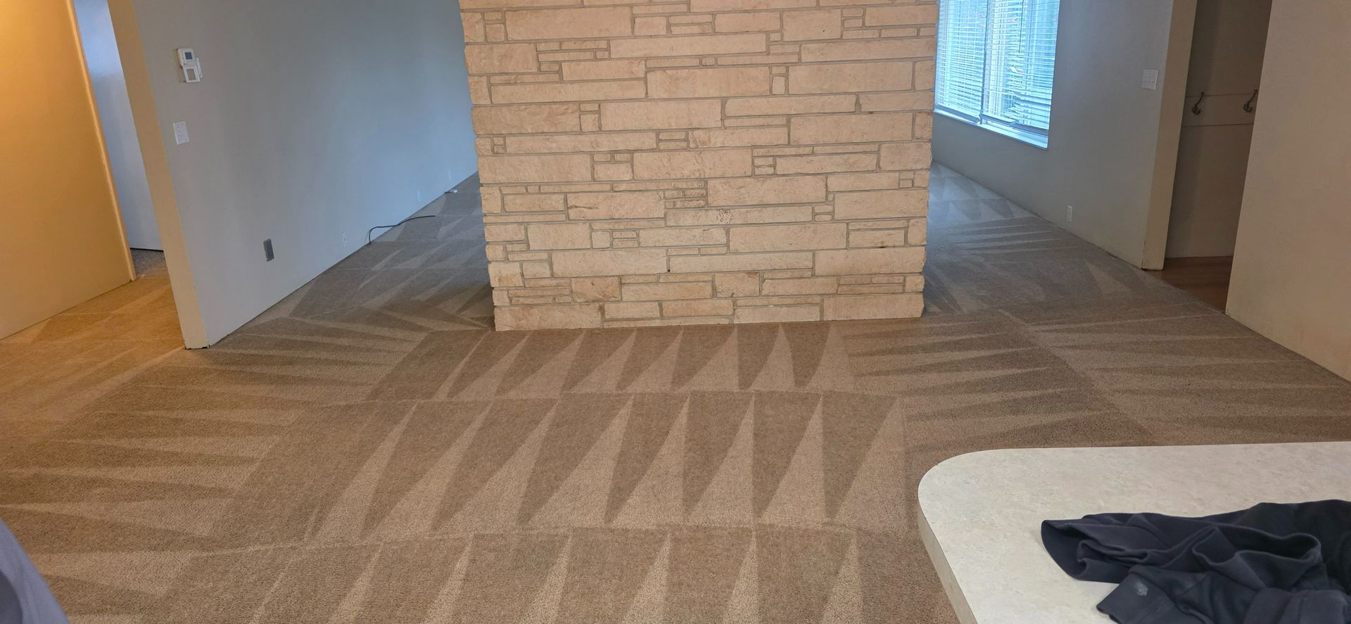 Empty carpeted room with a stone accent wall, hallway openings, and a sofa edge in the foreground