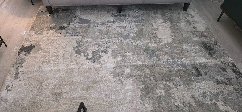Gray patterned rug on a light floor in a living room, with a sofa at the top edge.