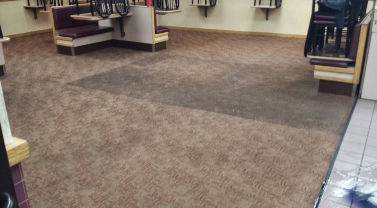 Empty carpeted room with tables and chairs along the walls and tiled floor at right