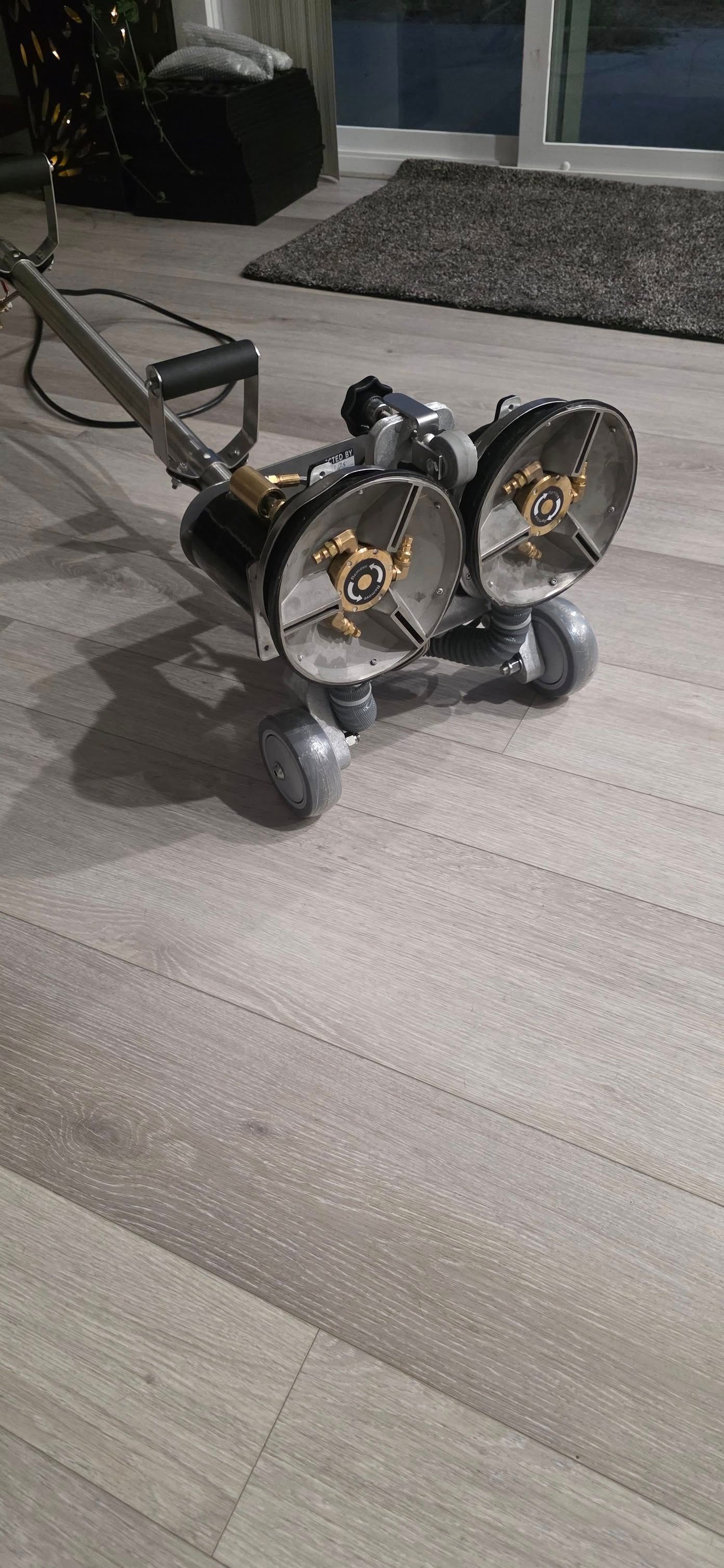 Black and silver dual-wheel lawn mower on a patio near a house window and gravel bed