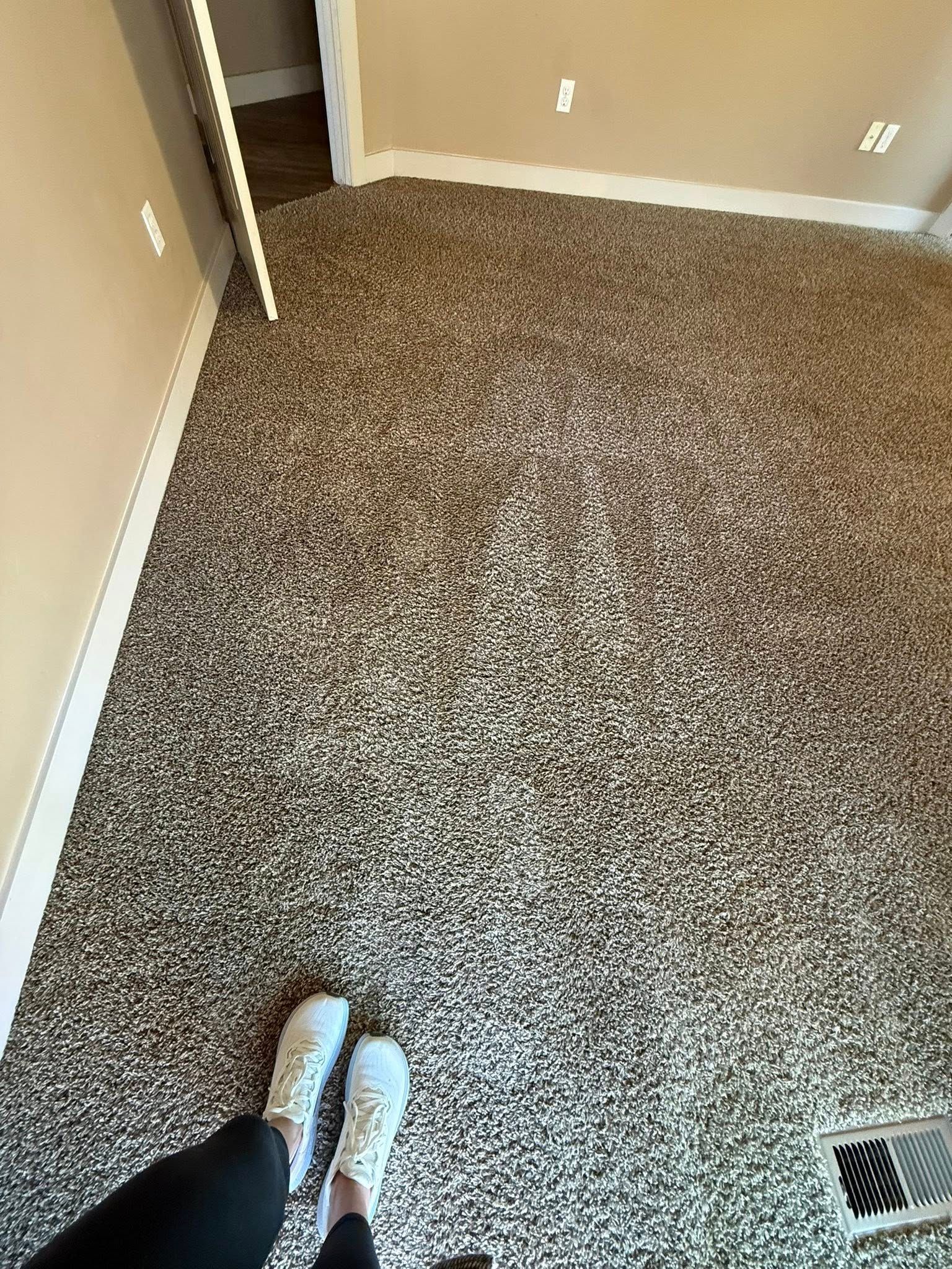 Carpeted empty room with tan walls, seen from a person’s feet near the doorway.