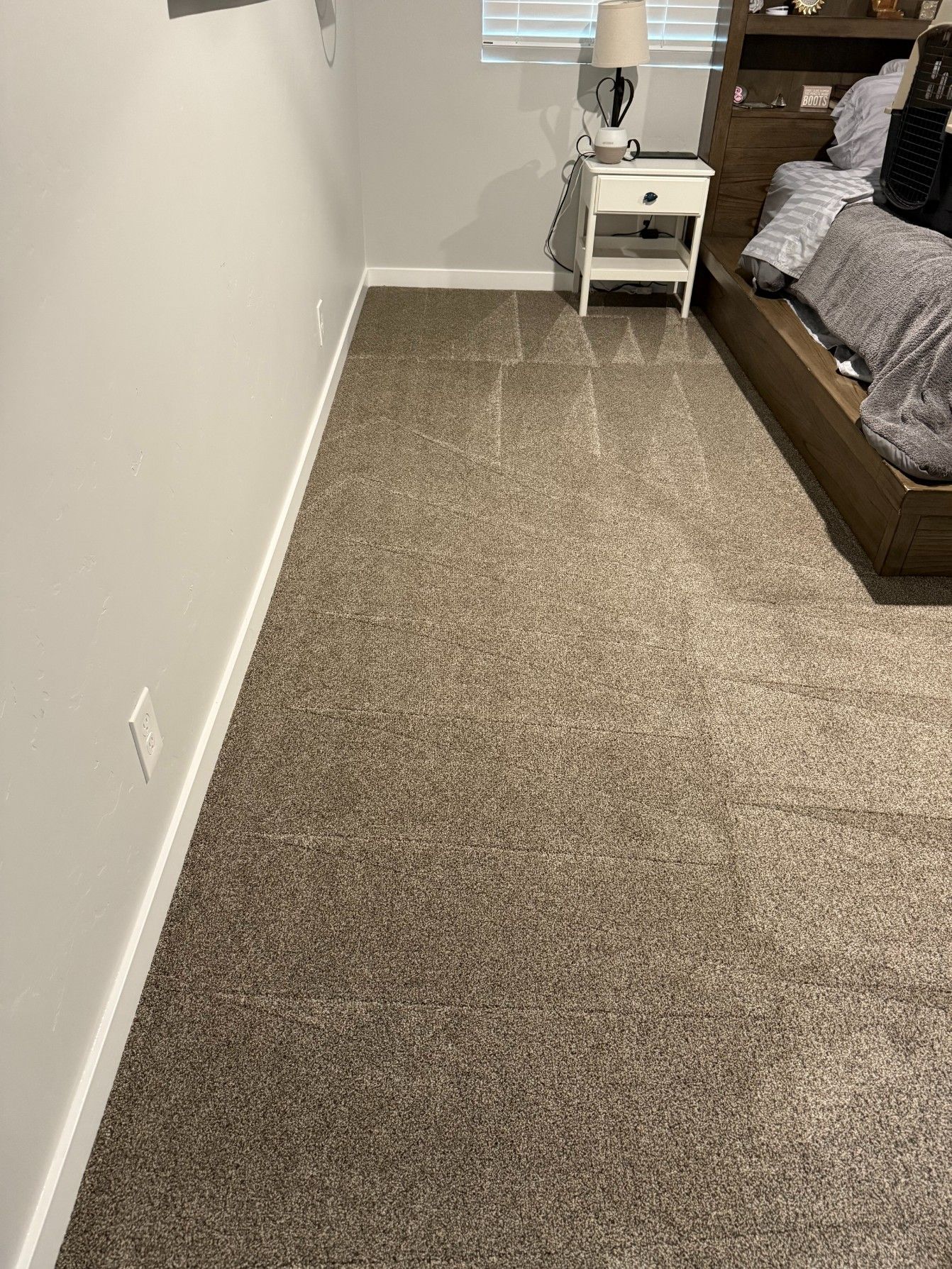 Empty carpeted bedroom with a bed, white nightstand, and chair beside the wall.