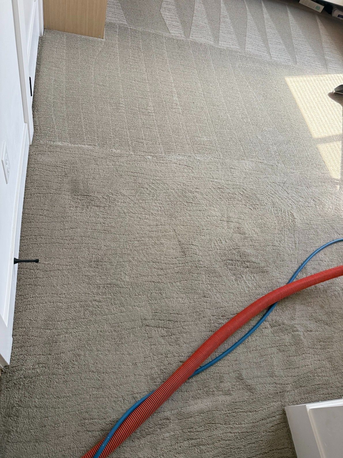 Carpeted floor with red and blue cables running diagonally near a white wall and doorway trim