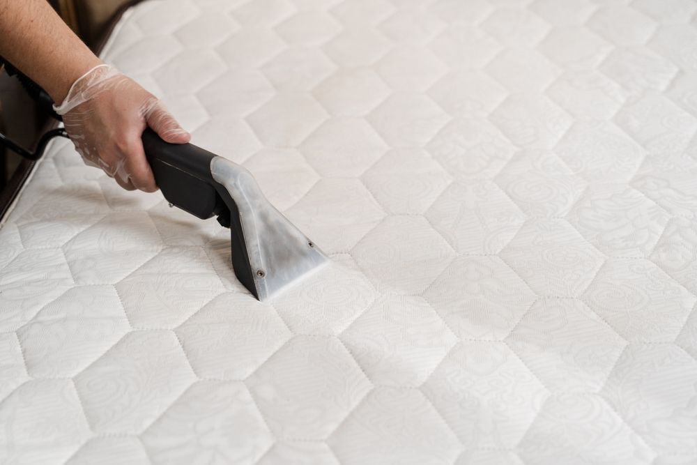 Person using a handheld vacuum on a white quilted mattress or upholstered surface