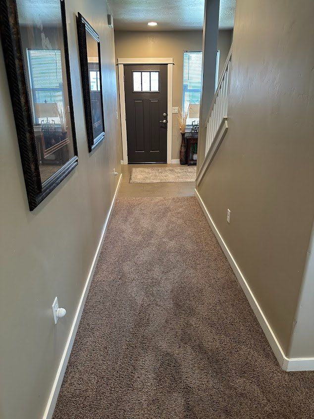 Narrow beige hallway with carpet, wall mirrors, and a dark front door at the end.