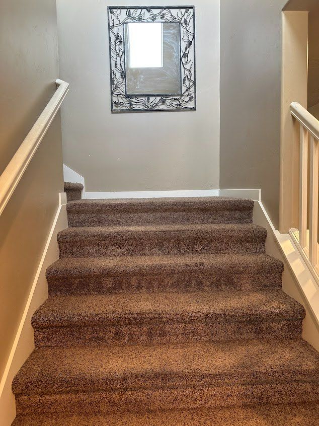 Carpeted staircase in a beige hallway with white railings and a decorative wall mirror at the landing