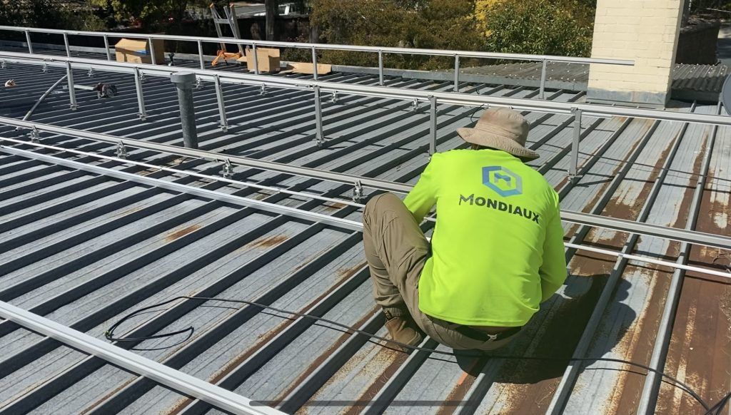 A man in a neon green shirt is kneeling on a roof.